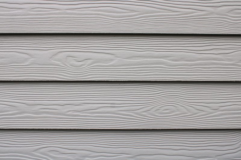 Close-up of horizontal light-gray wooden siding planks with pronounced wood grain and narrow gaps between boards.