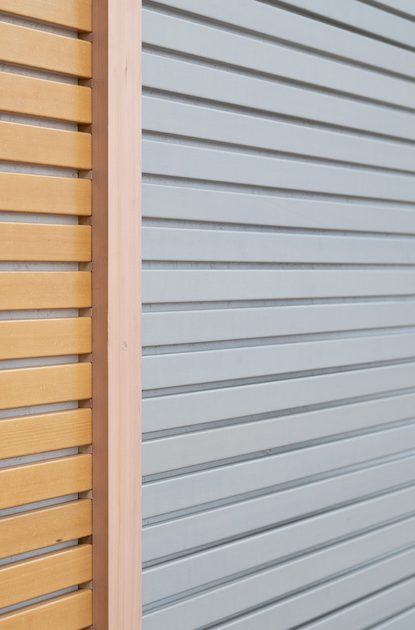 Close-up of three horizontal slatted panels in warm orange, pale gray, and dark gray, separated by vertical wooden dividers.
