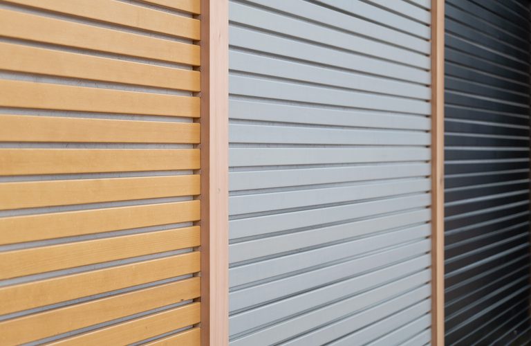 Close-up of three horizontal slatted panels in warm orange, pale gray, and dark gray, separated by vertical wooden dividers.