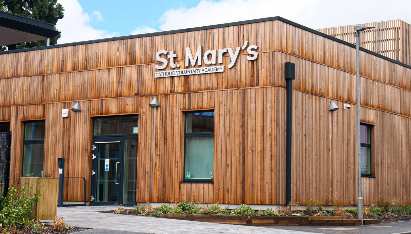 Modern school building with vertical wooden cladding, large windows, and minimalist signage for St. Mary’s Catholic Voluntary Academy.