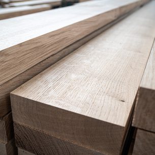 Stacked light brown wooden boards with visible grain and smooth planed surfaces, arranged in a pile.