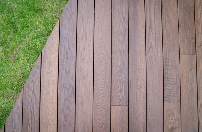 Brown wooden deck planks run across the frame with a green grassy lawn along the left edge.