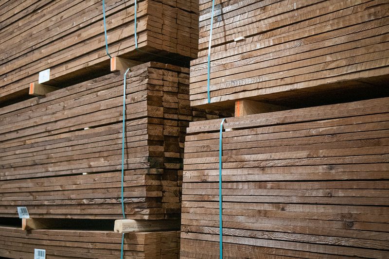 Stacks of brown wooden planks bound with blue straps, stacked high in a lumber yard.