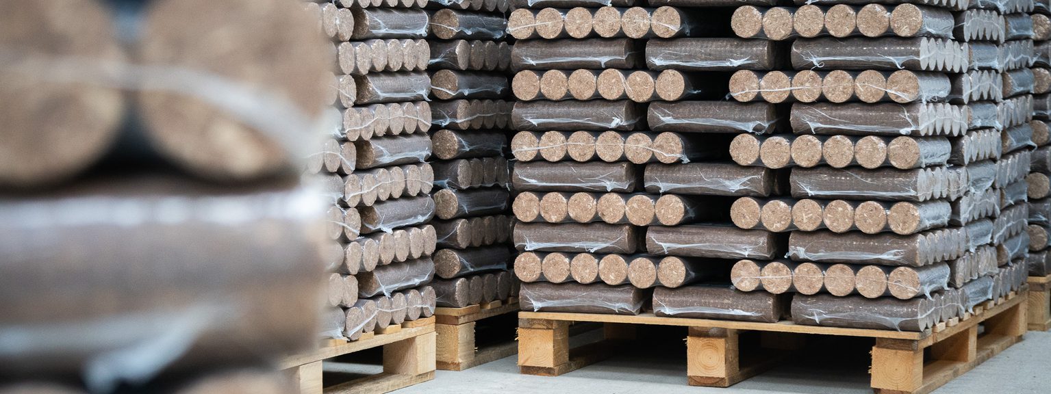 Stacks of round wooden dowels wrapped in plastic, stacked on pallets in a warehouse.