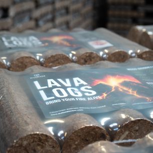 Stacks of lava logs wrapped in plastic, labeled LAVA LOGS with BRING YOUR FIRE ALIVE, set in a warehouse.