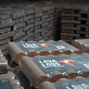 Stacks of lava logs in plastic-wrapped bundles on pallets inside a warehouse; labels read "LAVA LOGS" with a fiery flame graphic.