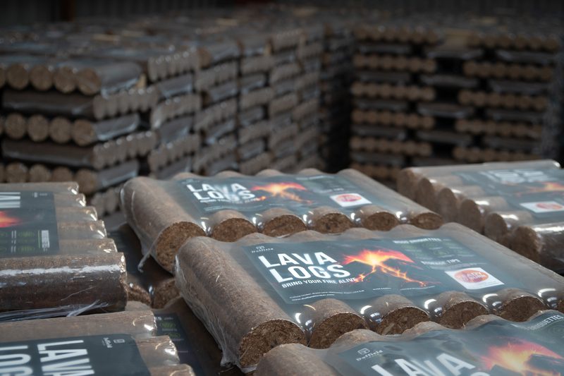 Stacks of lava logs in plastic-wrapped bundles on pallets inside a warehouse; labels read "LAVA LOGS" with a fiery flame graphic.