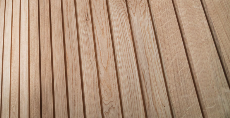 Close-up of light brown wooden deck planks with visible grain and knots, arranged diagonally with narrow gaps.