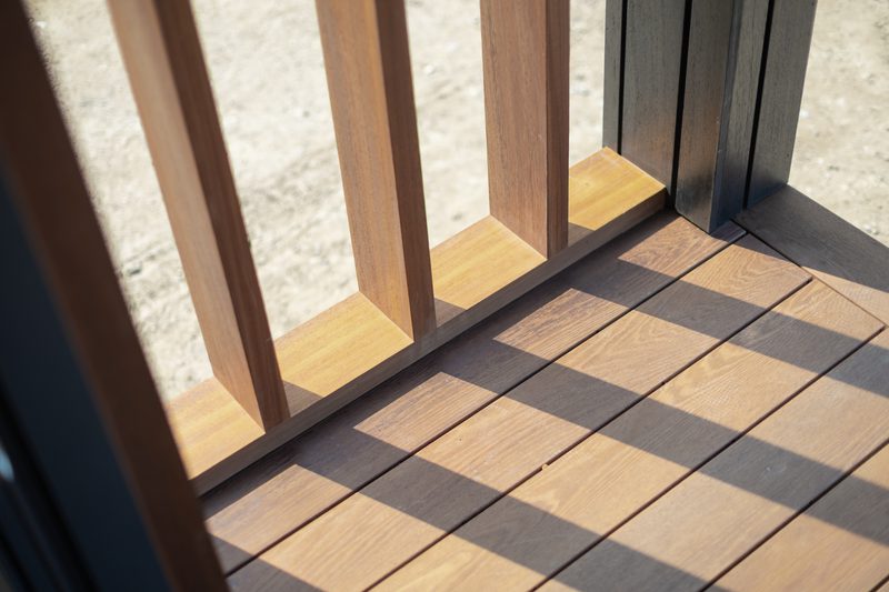 Sunlit wooden deck with vertical railing slats casting long shadows across the floorboards.