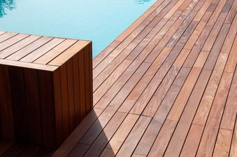 Wooden deck with diagonally laid planks and a rectangular wooden block near the pool edge, turquoise water visible at the top.
