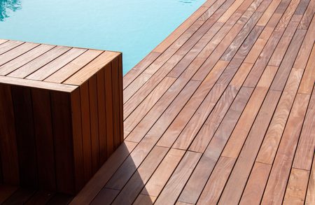 Wooden deck with diagonally laid planks and a rectangular wooden block near the pool edge, turquoise water visible at the top.