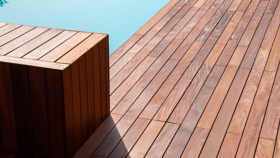 Wooden deck with diagonally laid planks and a rectangular wooden block near the pool edge, turquoise water visible at the top.