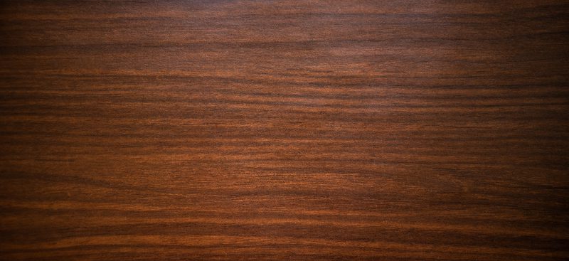 Close-up of a dark brown wood grain surface with polished texture and horizontal stripes.