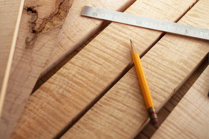 Close-up of light wooden planks with a metal ruler laid diagonally and a yellow pencil resting on the surface.
