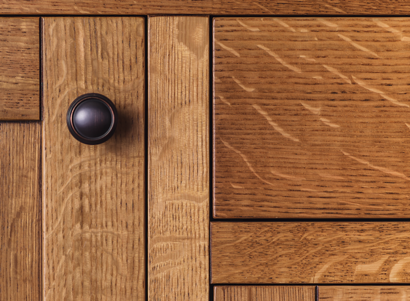 Close-up of a wooden cabinet door with a dark round knob on a vertical plank, surrounded by lighter wood panels with pronounced grain.