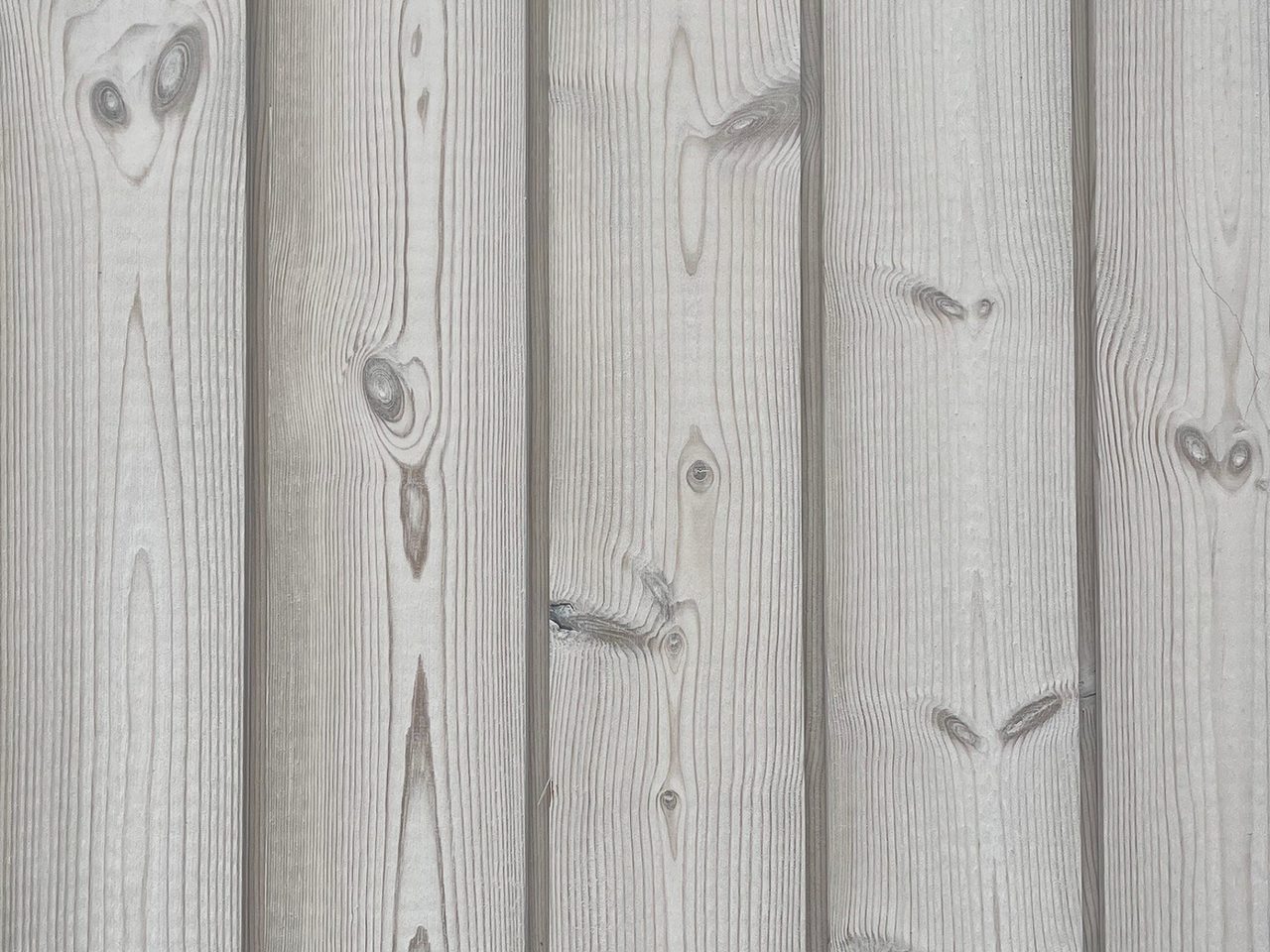 Close-up of vertical wooden planks with visible grain patterns and knots, showing a weathered gray surface.