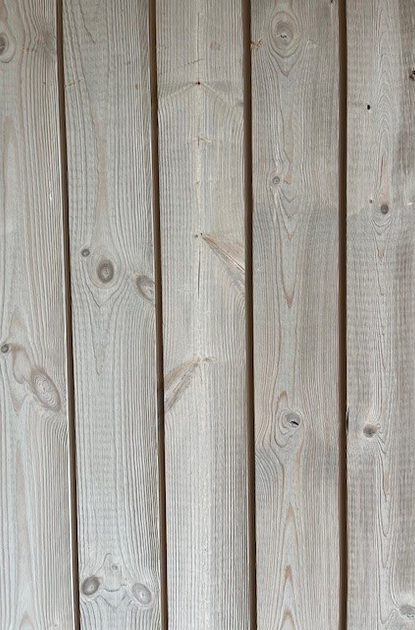 Close-up of vertical, weathered light-gray wooden planks with visible grain, knots, and narrow gaps between boards.