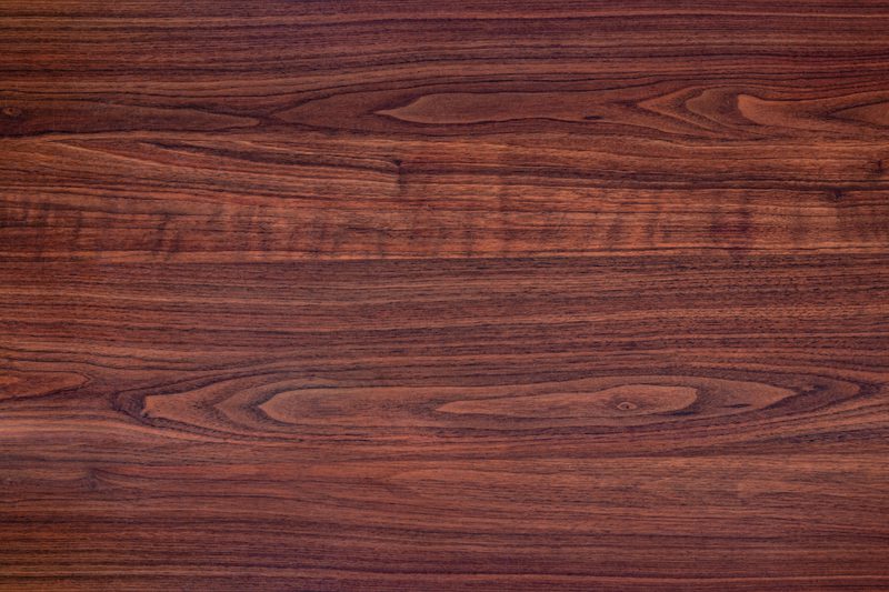 Close-up of a reddish-brown wood surface with visible grain patterns and natural knots.