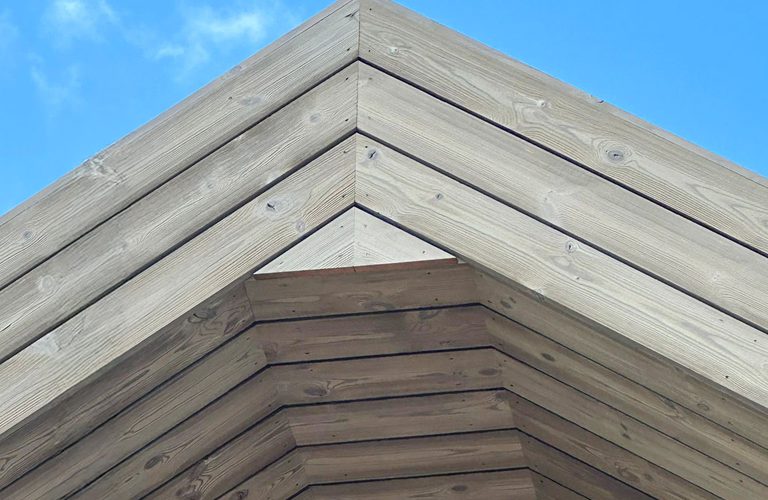 Low-angle view of a layered wooden gable roof above a brick wall, set against a clear blue sky.