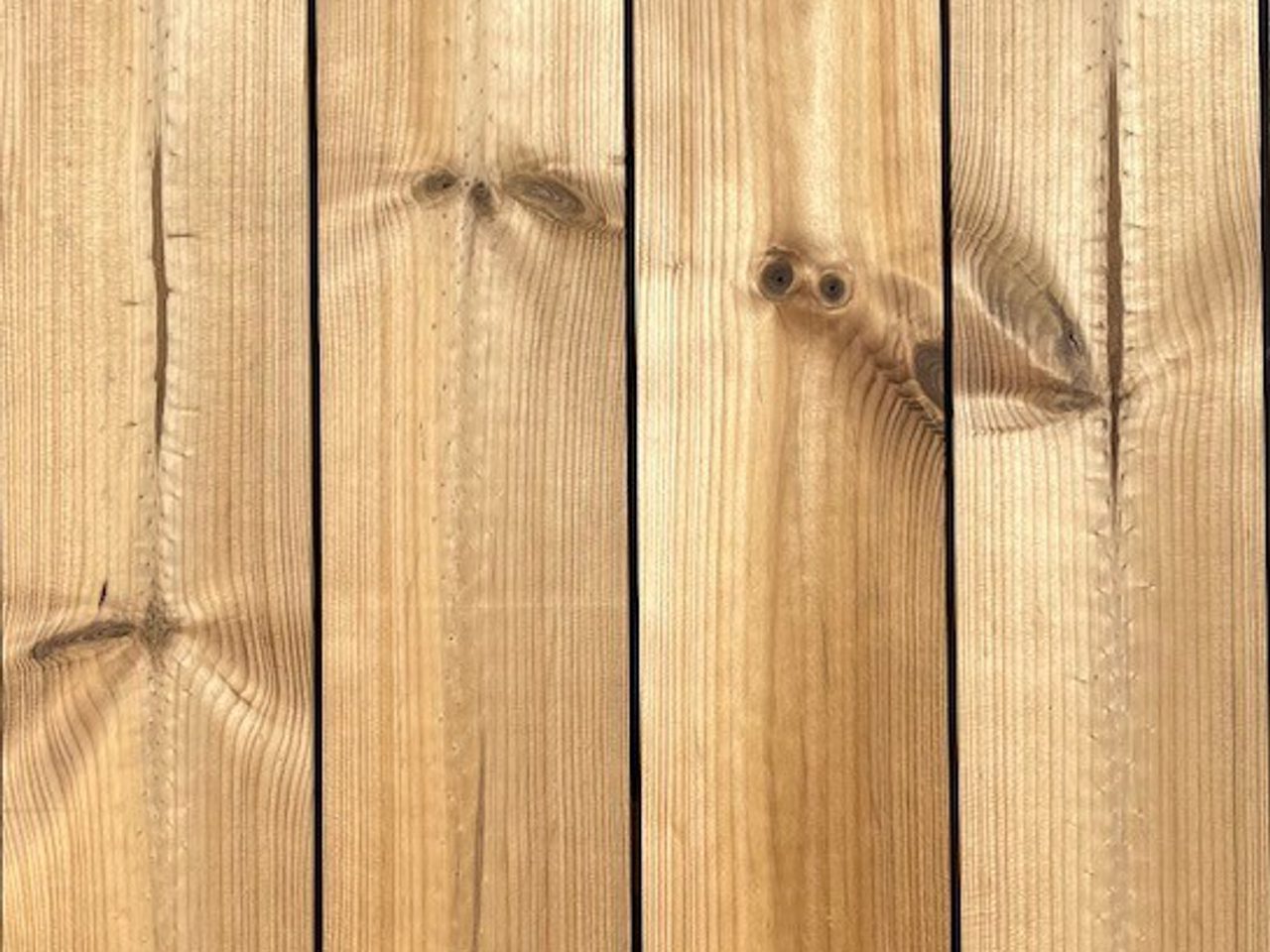 Close-up of vertical wooden boards with natural grain and knots, light brown color, and small nails along the planks.