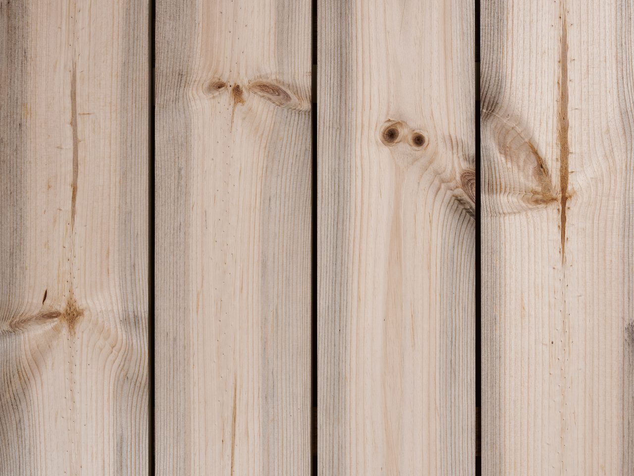 Close-up of vertical, light-colored wooden planks showing natural grain and knots, with narrow gaps between boards.