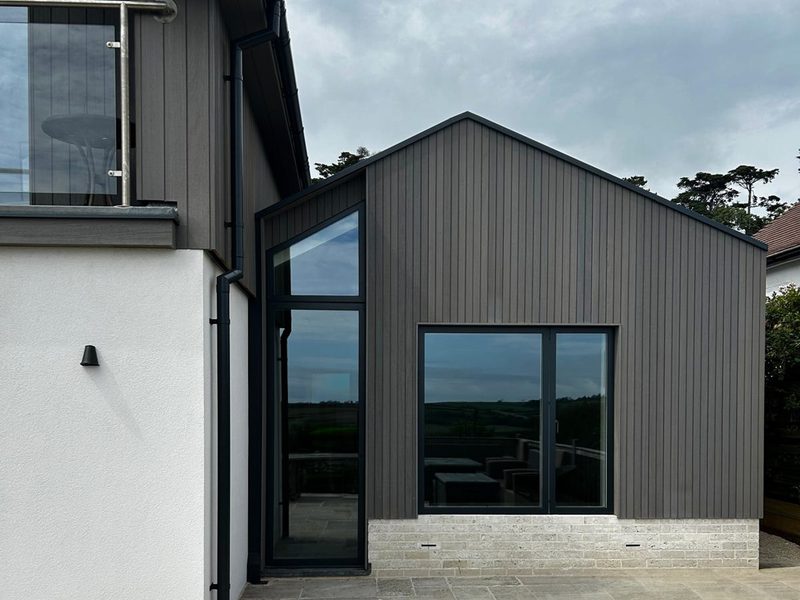 A modern house in Dorset, on the south coast of England, featuring Thermo-Ayous timber cladding in 'stone grey' with black-framed windows.