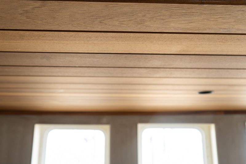 Wood-paneled ceiling with horizontal planks in warm tones; blurred interior with two rectangular windows and a small dark vent on the ceiling.