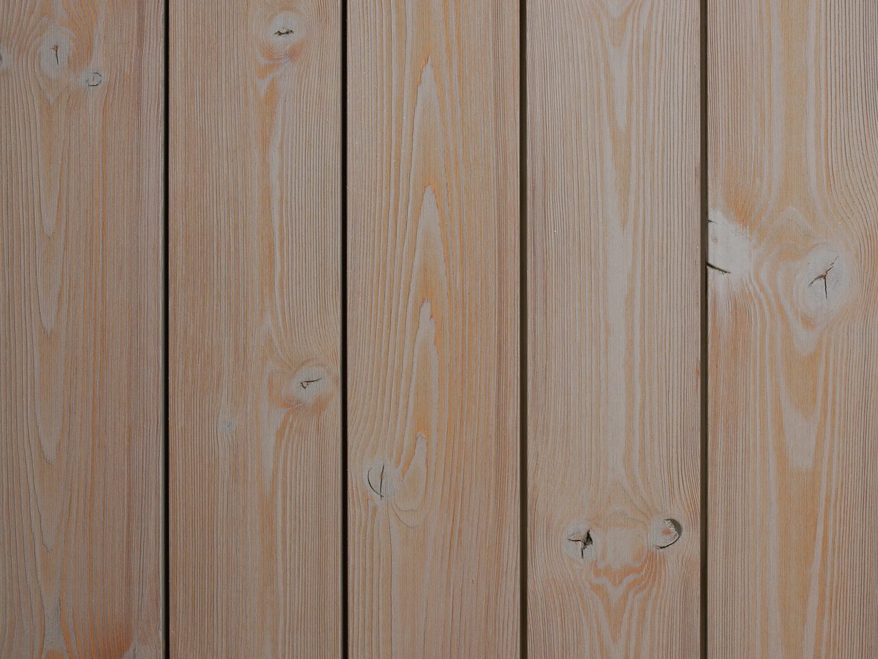 Close-up of vertical wooden planks with visible grain, knots, and narrow gaps, showing natural light-brown wood.