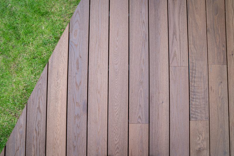 Brown wooden deck planks run along the right side, adjacent to a green grassy lawn on the left, with a diagonal seam between them.