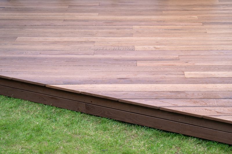 Brown wooden deck on a green lawn, with evenly spaced horizontal planks and a slightly raised edge.