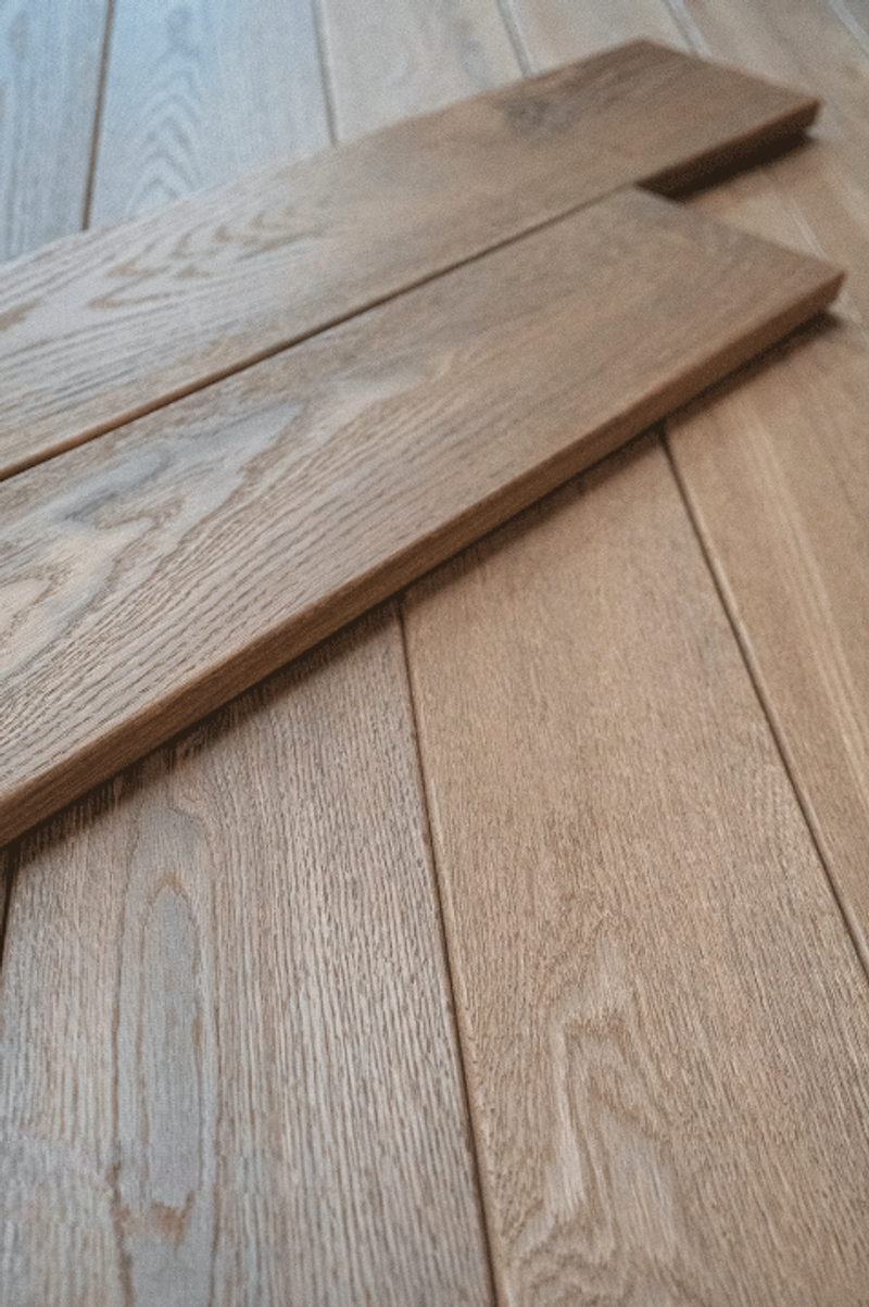 Close-up of light brown wooden floorboards with visible grain; two diagonal planks, one end notch-cut.