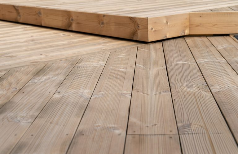 Close-up of light brown wooden deck boards with a small stack of lumber resting on the edge.
