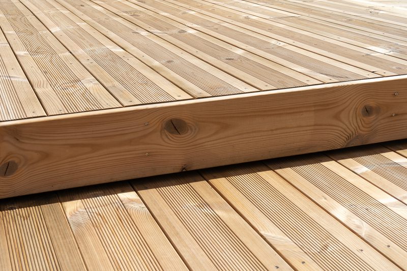 Close-up of a light-brown wooden deck with a raised edge; visible grain patterns, screws along the edge, and evenly spaced planks.
