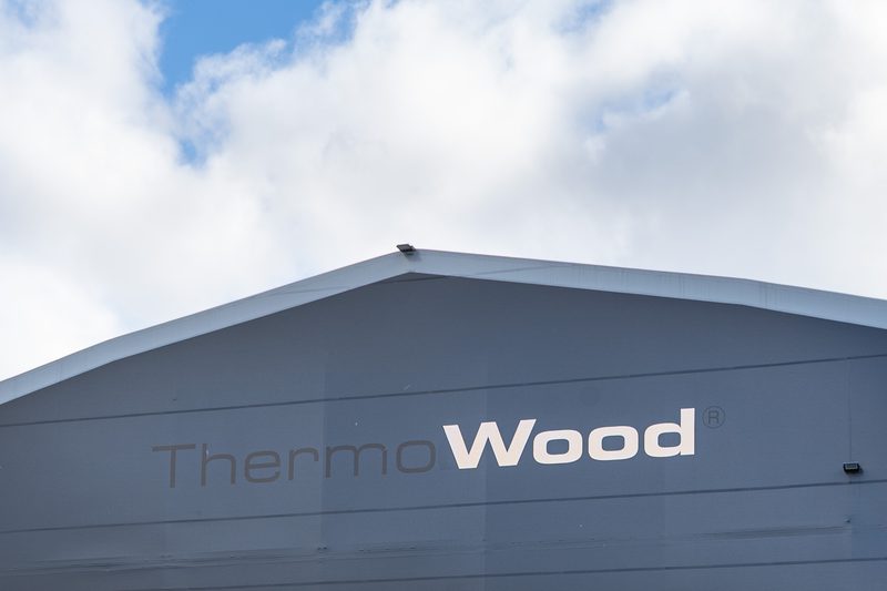 Blue-gray industrial building with a white roof edge displaying the ThermoWood logo, under a partly cloudy sky.