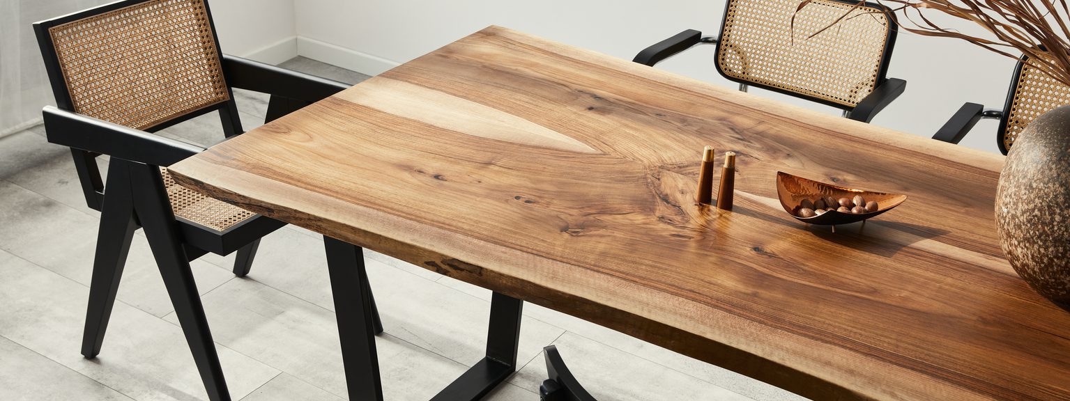 A wooden dining table with black metal legs, surrounded by caned chairs; brass spice grinders, a wooden bowl with nuts, and dried branches.