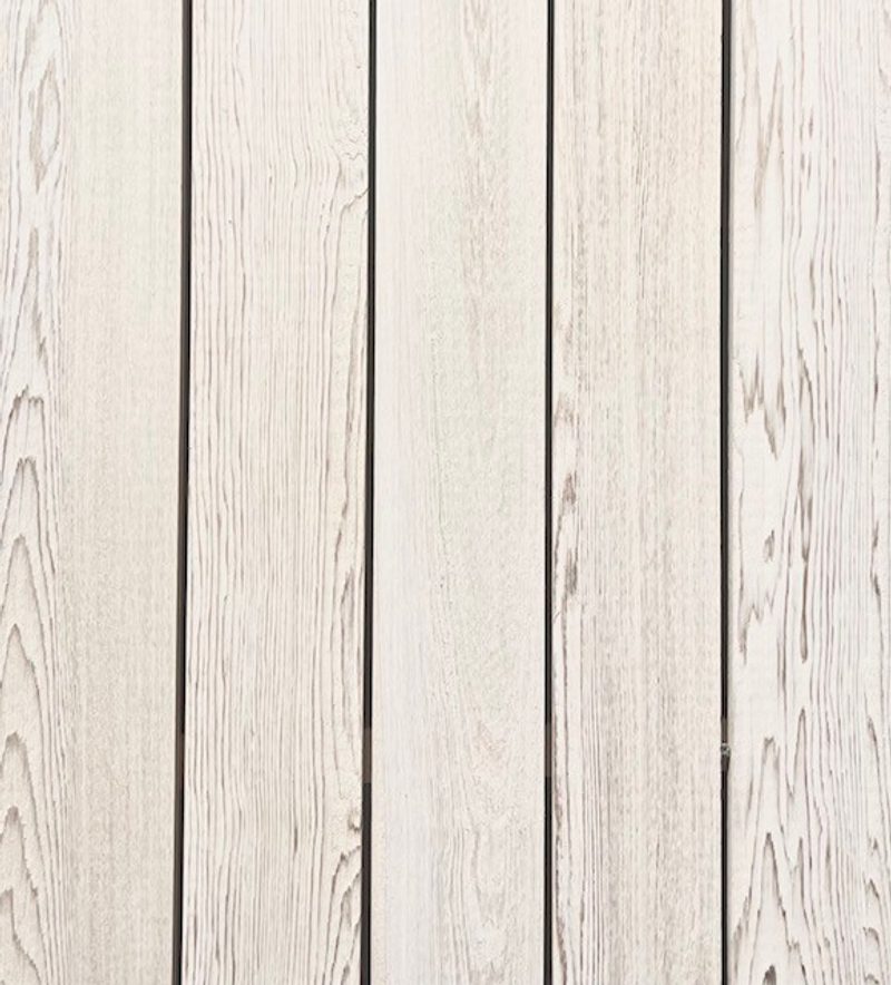 Vertical light wood planks with visible grain and narrow gaps, forming a pale wooden panel background.