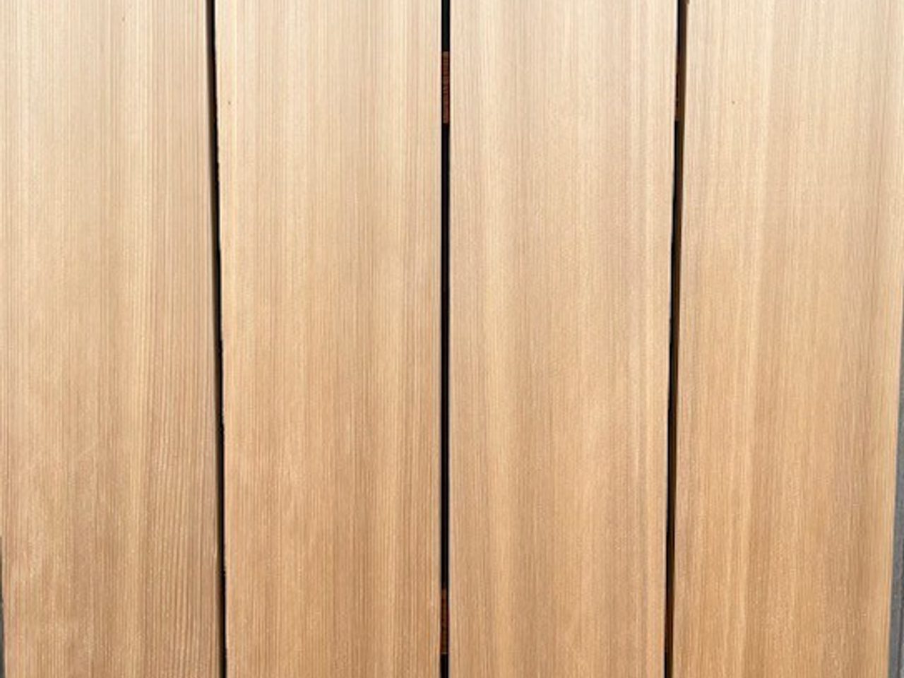 Close-up of five vertical light-brown wooden planks with visible grain, small knots, and screws at the edges.