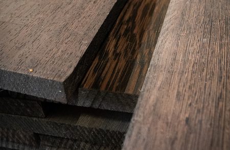 Close-up of dark wooden planks stacked together, displaying wood grain, varying finishes, and rough edges.