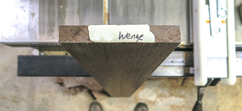 Top-down view of a conical bristle brush attached to a metal frame, with a torn tape label bearing handwritten text on its flat top.
