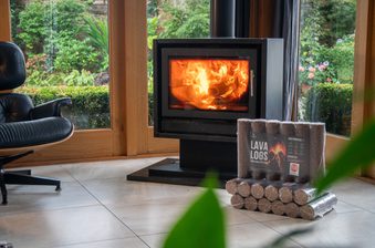Cozy living room with a black wood stove burning, a black leather lounge chair on the left, large glass windows showing a garden and lava logs.