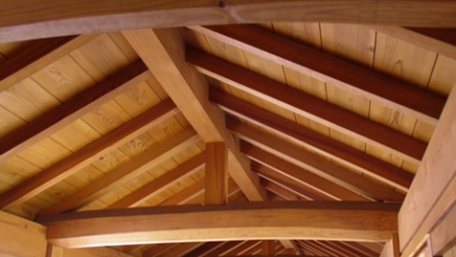 Interior view of a wooden ceiling with exposed beams and trusses, warm planks, and natural light in a rustic cabin.