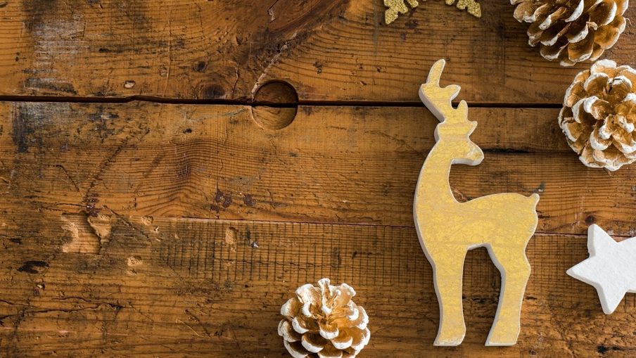 Gold reindeer silhouette ornament on a rustic wooden table, with frosted pinecones and a white star cutout nearby.