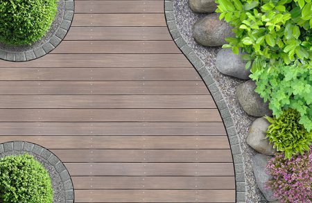 Top-down view of a curved wooden deck path edged with gray stones, with rocks and lush green shrubs on the right and round planters on the left.