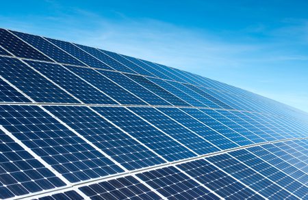 Vast solar farm with parallel rows of blue photovoltaic panels angled toward the horizon under a clear blue sky.