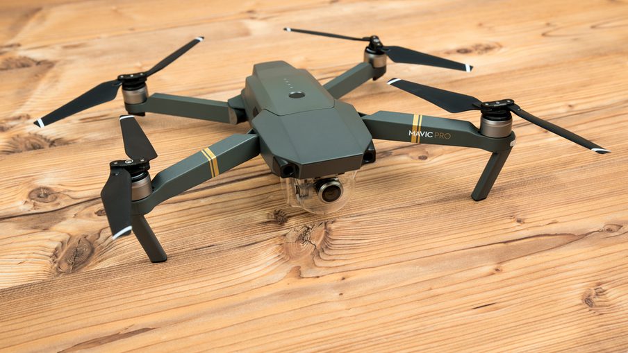 Mavic Pro quadcopter with four folding arms and propellers sits on a wooden floor; camera mounted beneath the body.
