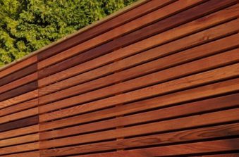 Close-up of a reddish-brown wooden slat wall with horizontal slats; green trees visible in the upper left.