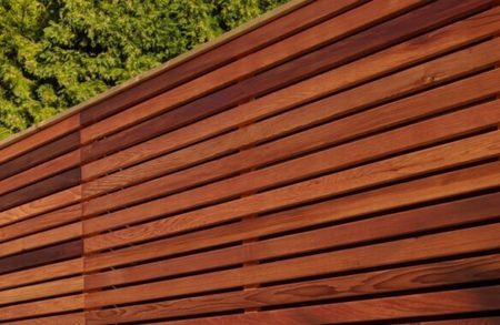 Close-up of a reddish-brown wooden slat wall with horizontal slats; green trees visible in the upper left.