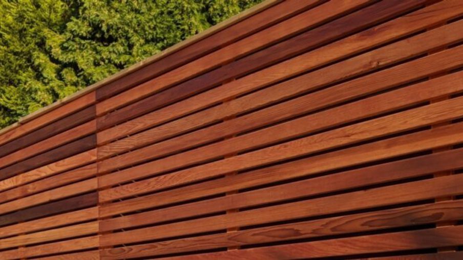 Close-up of a reddish-brown wooden slat wall with horizontal slats; green trees visible in the upper left.