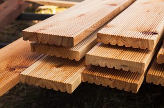 Stacks of pale pine boards with tongue-and-groove edges, outdoors on a grassy surface.