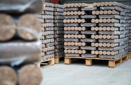 Stacks of round-ended wooden timbers wrapped in plastic, stacked on wooden pallets in a warehouse.